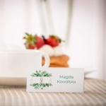 Białe eleganckie winietki na komunię z zielonymi liśćmi